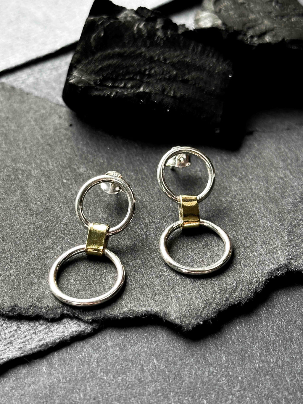A pair of silver link earrings, with one smaller circle and one larger circle, connected by a gold-toned chunky link.