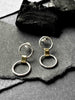 A pair of silver link earrings, with one smaller circle and one larger circle, connected by a gold-toned chunky link.