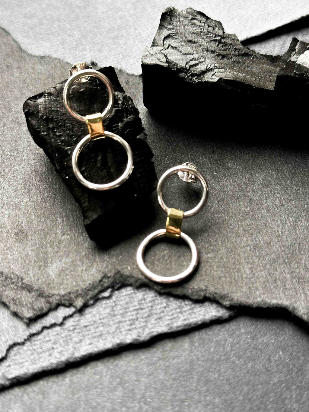 A pair of silver link earrings, with one smaller circle and one larger circle, connected by a gold-toned chunky link.