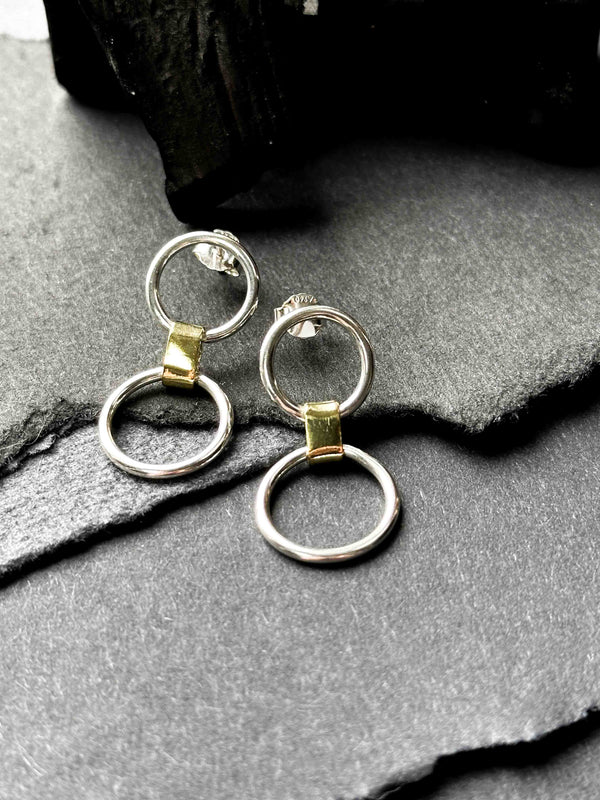 A pair of silver link earrings, with one smaller circle and one larger circle, connected by a gold-toned chunky link.