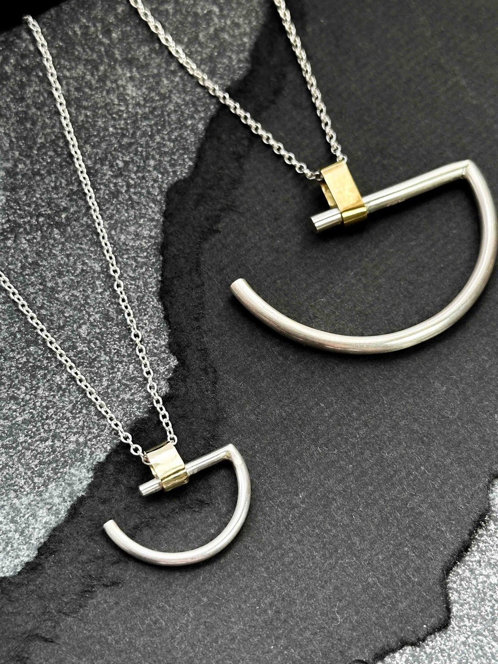 A large and a small minimalist semi-circle pendant in silver with contrasting gold-coloured bar bail on a chunky chain.