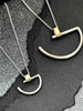 A large and a small minimalist semi-circle pendant in silver with contrasting gold-coloured bar bail on a chunky chain.