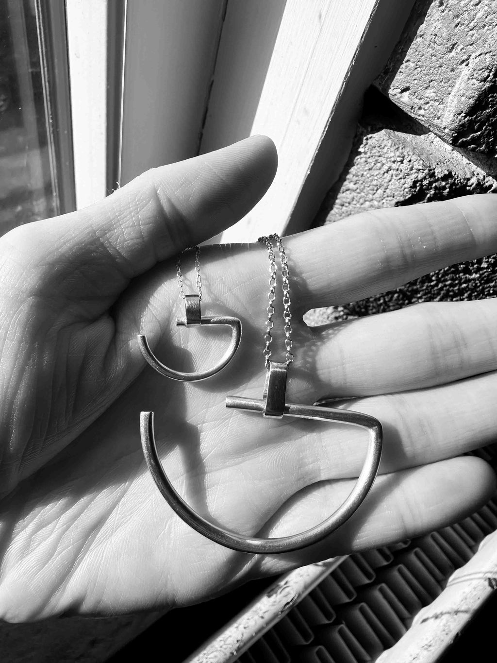A large and a small minimalist semi-circle pendant in silver with contrasting gold-coloured bar bail on a chunky chain.