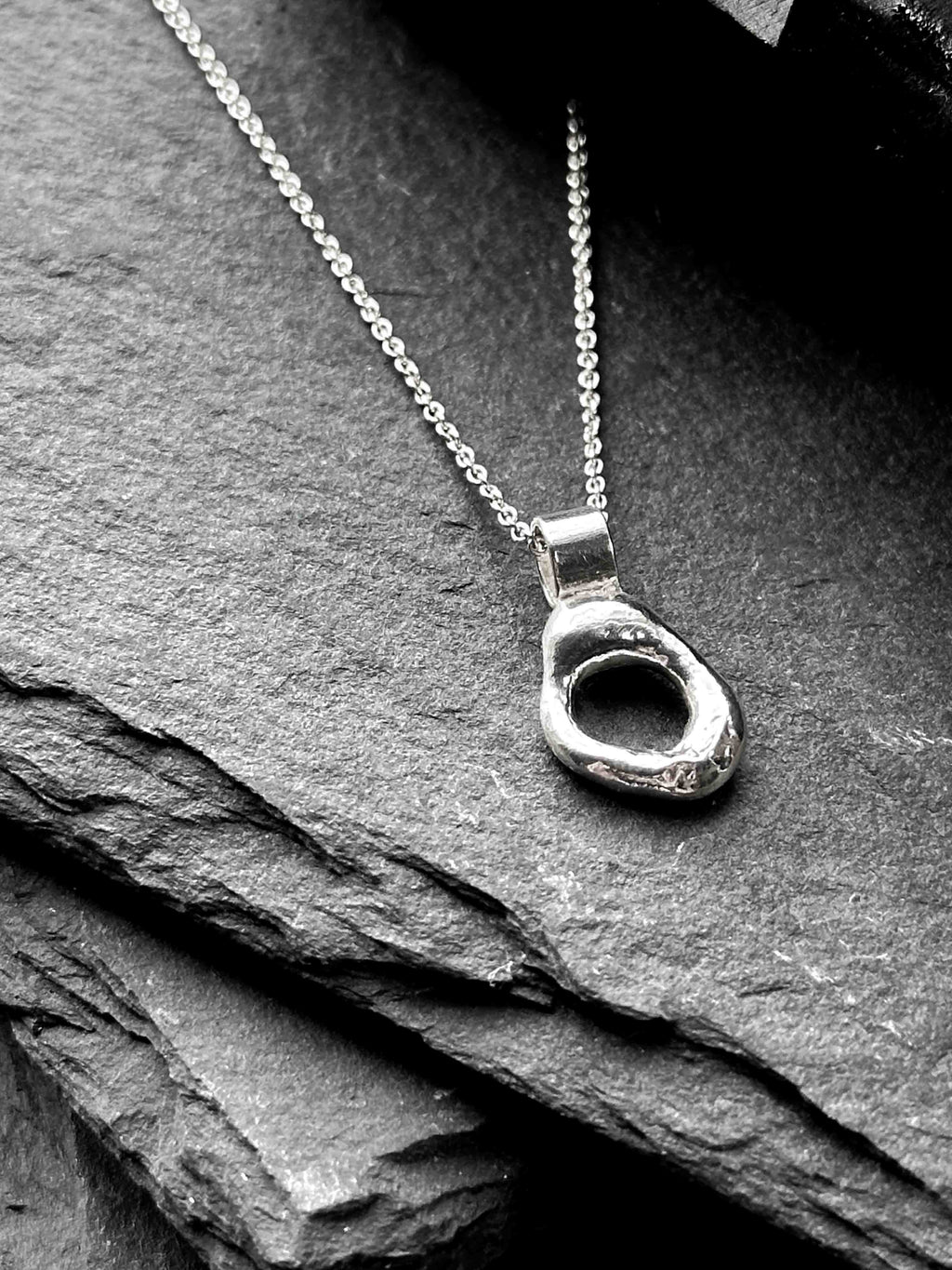 A silver necklace with a textured, organic-shaped molten circle pendant