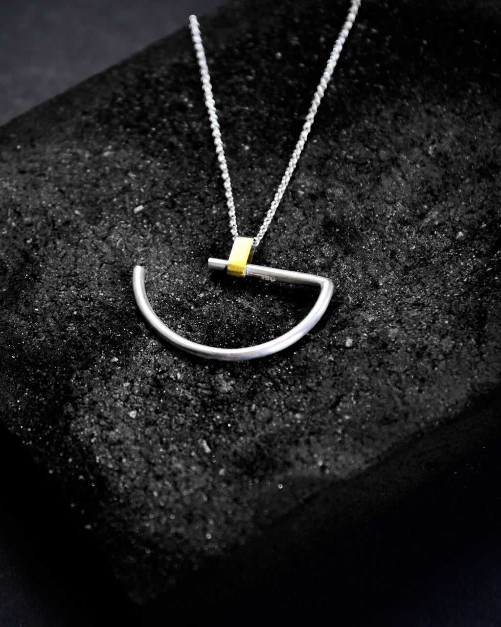 A large minimalist semi-circle pendant in silver with contrasting gold-coloured bar bail on a chunky chain.