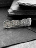 A hand wearing a large, rectangular textured silver ring with a ripped, organic edge and rippling molten texture.