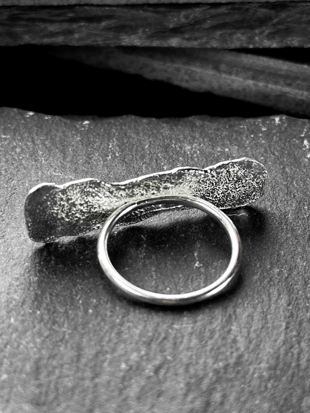 A large, rectangular textured silver ring with a ripped, organic edge and rippling molten texture.