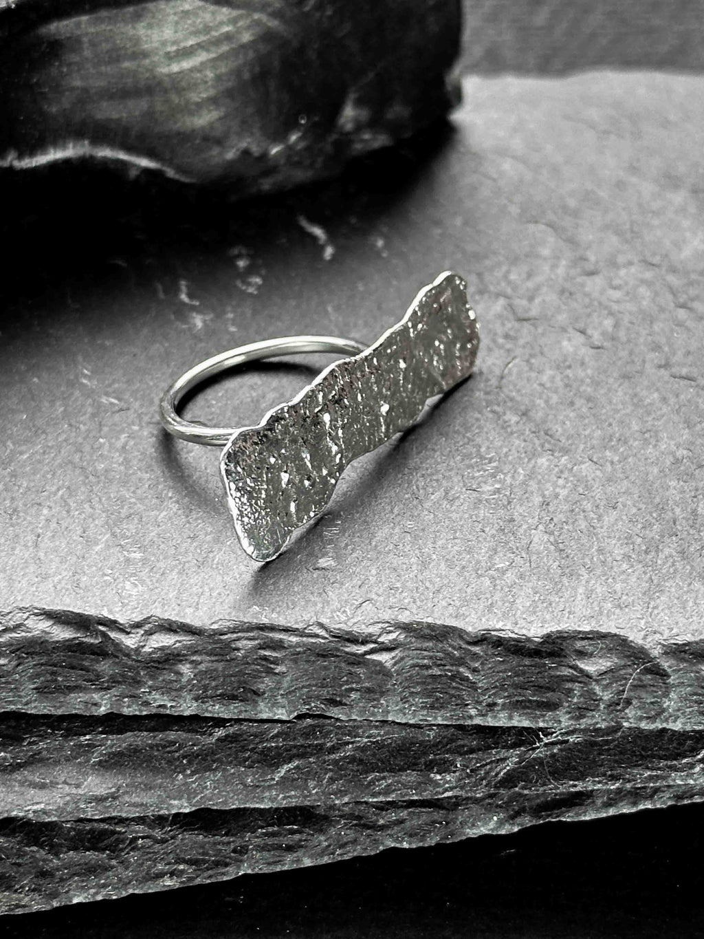 A large, rectangular textured silver ring with a ripped, organic edge and rippling molten texture.