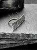 A large, rectangular textured silver ring with a ripped, organic edge and rippling molten texture.