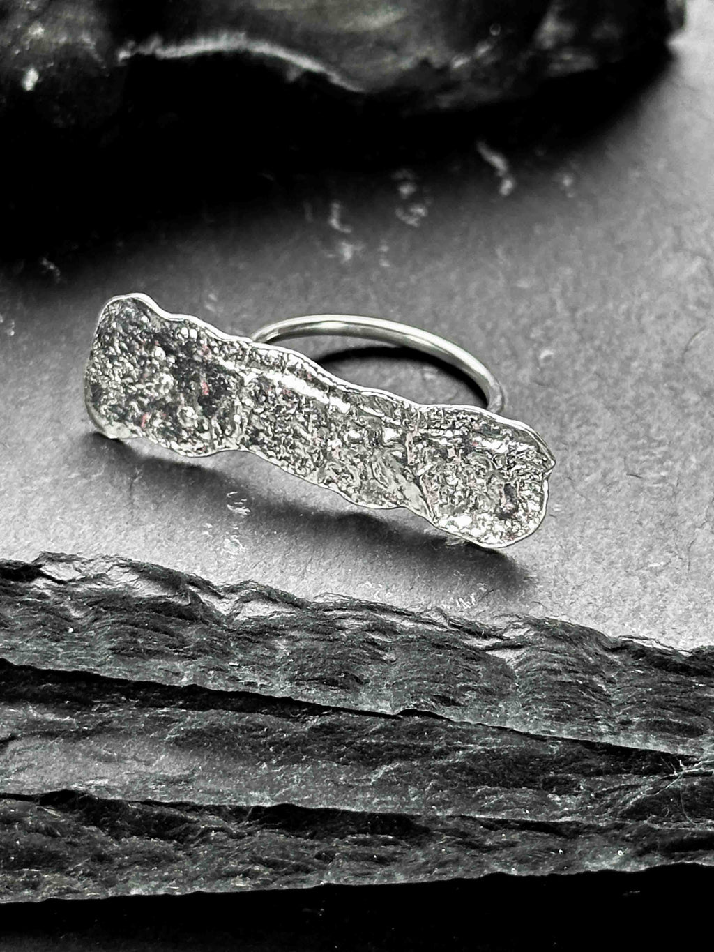 A large, rectangular textured silver ring with a ripped, organic edge and rippling molten texture.