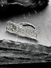 A large, rectangular textured silver ring with a ripped, organic edge and rippling molten texture.